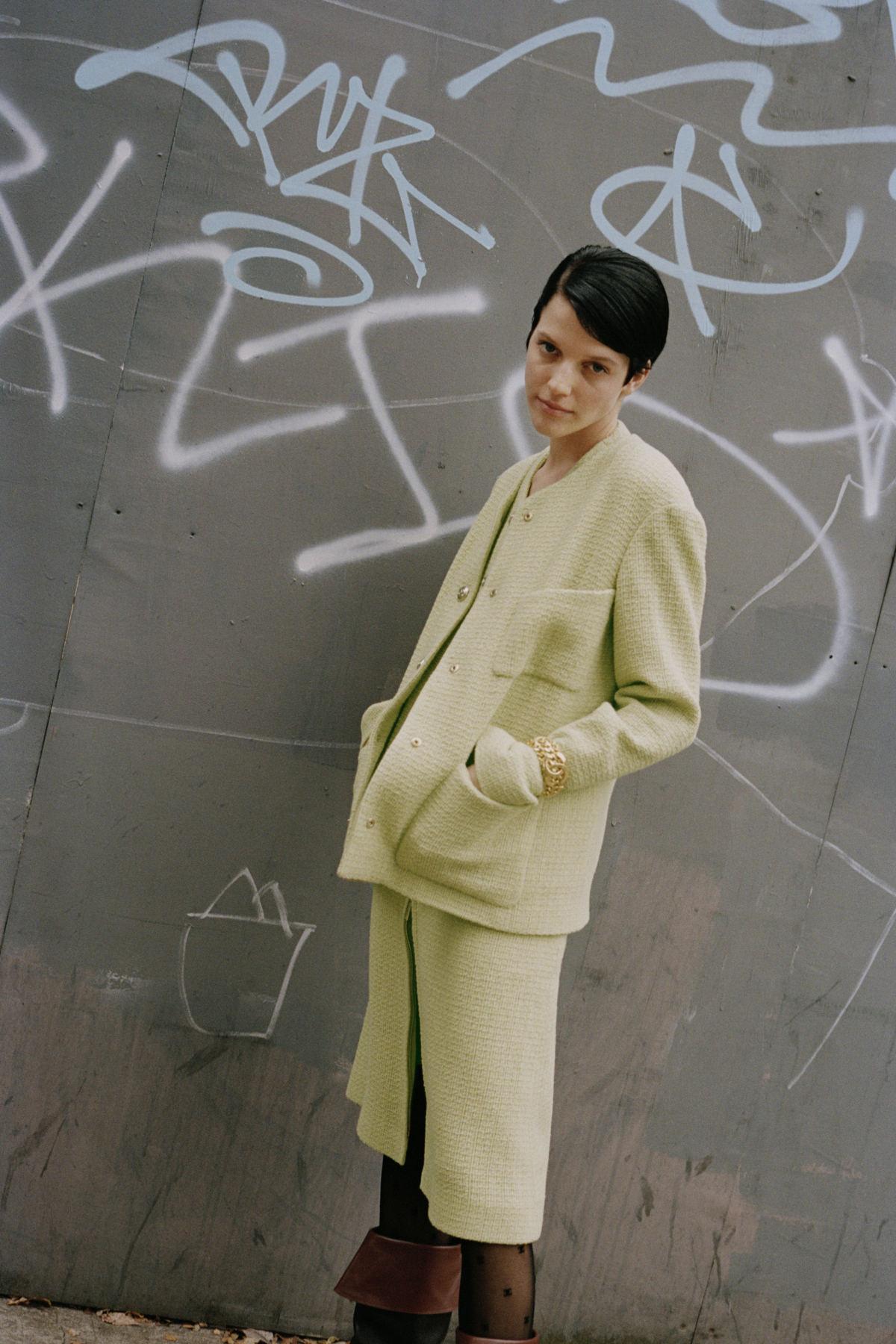 black haired model standing in front of graffiti in green chanel suit